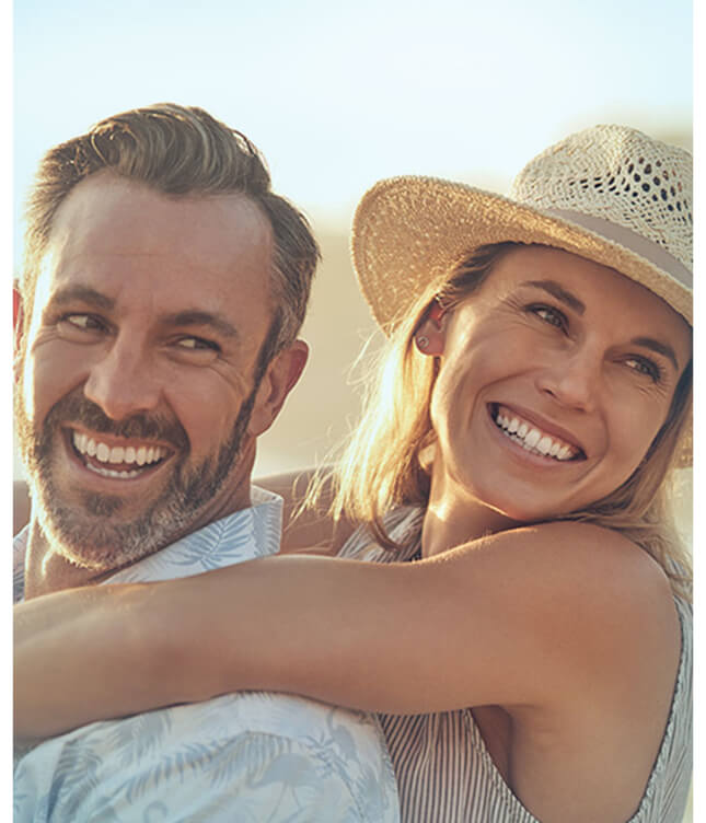 Smiling couple outdoors in warm sunlight, embracing and looking off into the distance